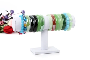 Close-up of white T-bar jewelry display rack holding assorted jade bangles and beaded bracelets