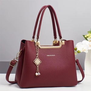 Detail der burgunderroten Handtasche mit Lychee-Leder, Gold-Hardware und Perlenanhänger