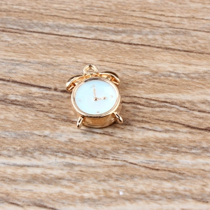 Detailed view of a gold-tone alarm clock charm with white dial on wood background
