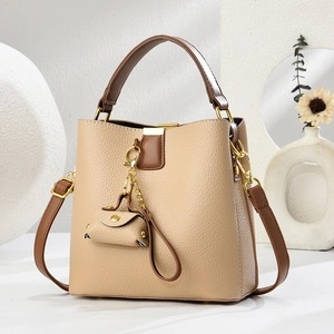 Sac seau beige avec poignées marron, finitions dorées et pendentif de sac décoratif