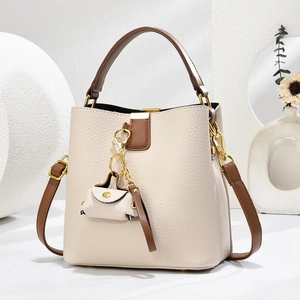 Détail du sac seau beige à motif litchi avec anses brunes et finitions dorées
