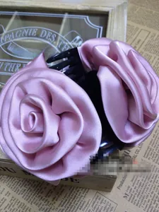 Detail of pink satin fabric rose hair clip with elegant layered petals and black comb base