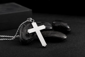 Close-up of a silver stainless steel cross pendant with brushed finish on dark background
