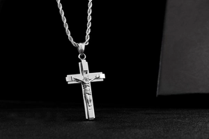 Detail view of silver stainless steel crucifix pendant with twist chain on dark background