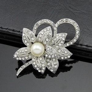 Macro detail of a silver flower brooch featuring pavé crystals and a central large pearl