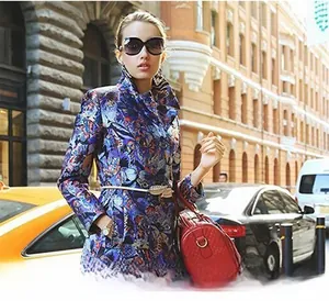 Detailed view of an ornate gold leaf buckle on a navy floral coat with red quilted bag