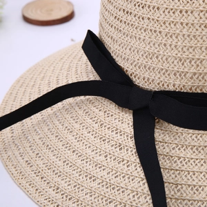 Detail of beige straw hat featuring fine weave texture and elegant black ribbon bow