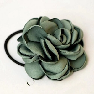 Elegant dark green camellia fabric hair tie with layered satin petals on a magazine