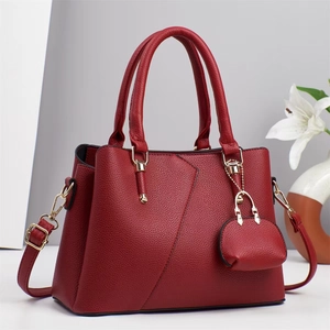 Detail of burgundy lychee leather handbag with gold hardware and mini bag charm