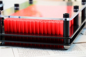 Detail view of red 3D pin art clone hand mold with plastic pins and transparent acrylic frame