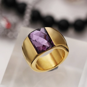 Macro detail of a wide gold-plated ring featuring a large faceted rectangular purple crystal