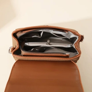 Detail view of brown crossbody bag with multi-compartment interior and silver hardware