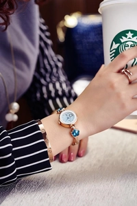 Rose gold watch with blue flower gems and matching bracelet on woman holding coffee