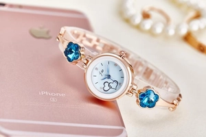 Detail of rose gold quartz watch featuring blue gradient heart dial and crystal flower band