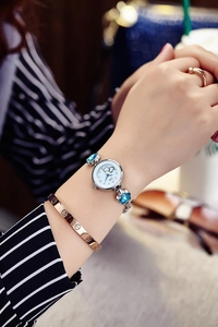 Close-up of a silver watch with heart patterns and blue floral accents on the wrist