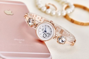 Detail of rose gold watch with heart dial and crystal flower bracelet next to a phone