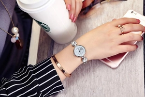 Close-up of a silver watch with heart dial and rhinestone strap on a woman wrist