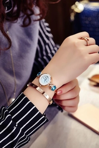 Detail of elegant gold watch with white dial, floral accents, and screw motif bracelet