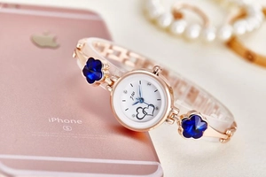 Detail of rose gold steel watch strap with clover charms and white dial showing heart motif