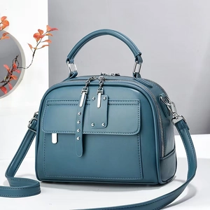 Macro detail of dark teal satchel bag showing premium leather texture and silver rivets