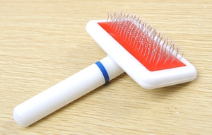 Detail of pet slicker brush with stainless steel needles and ergonomic handle on wood floor