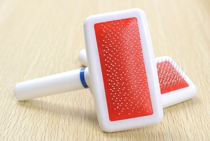 Close-up of pet slicker brush with fine metal needles on red rubber pad for fur grooming