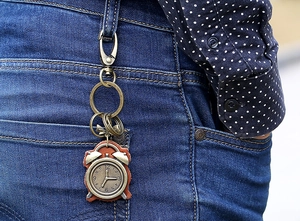 Detail of vintage bronze clock keychain with brown leather strap clipped on denim jeans