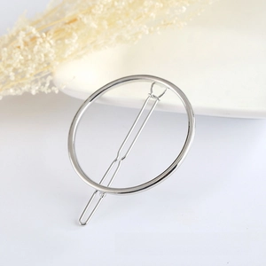 Minimalist silver circular metal hair clip with a smooth polished finish on a white tray
