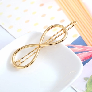 Macro view of a gold-plated infinity symbol hair clip on a minimalist ceramic plate