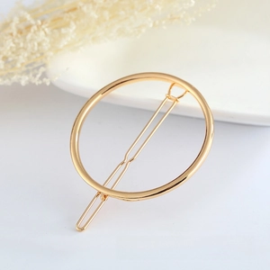 Close-up of a minimalist golden circular geometric hair clip on white porcelain