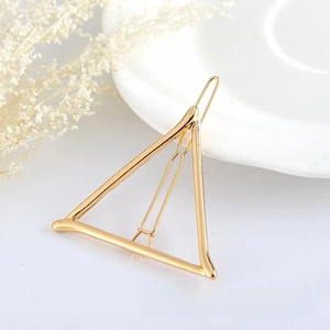 Detailed close-up of a golden geometric triangle hair clip on a white ceramic plate