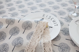Linen napkin with grey tree pattern and beige lace trim on a matching tablecloth