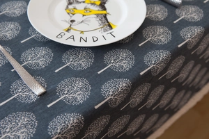 Detail of dark grey linen tablecloth with white tree patterns and fox motif ceramic plate