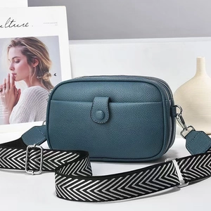Blue lychee leather mini crossbody bag with wide woven strap on a white surface