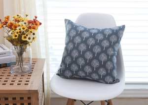 Detail of blue linen throw pillow with white tree pattern on a modern white chair
