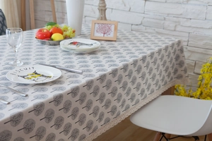 Close-up of beige linen tablecloth featuring grey tree patterns and delicate lace edges