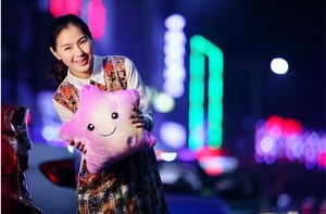 Close-up of pink glowing star plush pillow with LED lights held by a woman at night