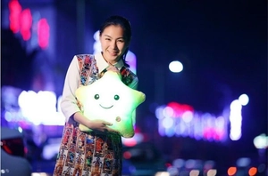 Star plush pillow with glowing LED light effect held by model in nighttime setting