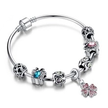 Detail of silver unicorn bracelet with blue butterfly, pink clover and crown charms