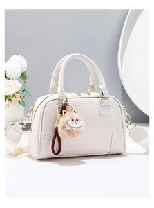 Detail of cream white leather boston bag with gold hardware and plush cat charm