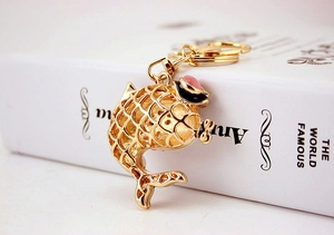 Detailed close-up of a golden metal carp fish keychain with colorful enamel on a book