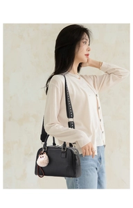 Detail of black lychee leather bag with a geometric pattern strap and cat charm on model
