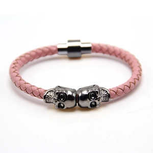 Close-up of pink braided leather bracelet featuring black skull charms and magnetic clasp