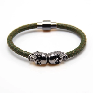 Close-up of olive green braided leather bracelet with dual metal skulls and magnetic clasp
