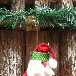 Detail of plush Santa Claus ornament with green S-hook hanging on festive background