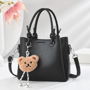 Detail of black lychee leather handbag with knotted handle and cute bear charm pendant