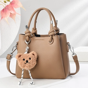 Detail of a brown lychee-grain leather handbag featuring a cute plush bear charm
