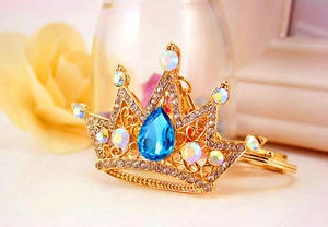 Close-up of golden crown keychain with blue teardrop gemstone and sparkling crystals