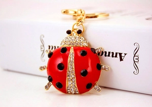 Detailed view of red ladybug keychain with rhinestones hanging on a white book edge