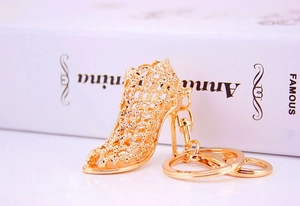 Detailed view of a gold-toned hollow mesh high heel shoe keychain next to a book